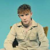 A guy sat looking towards the camera in front of a blue backdrop